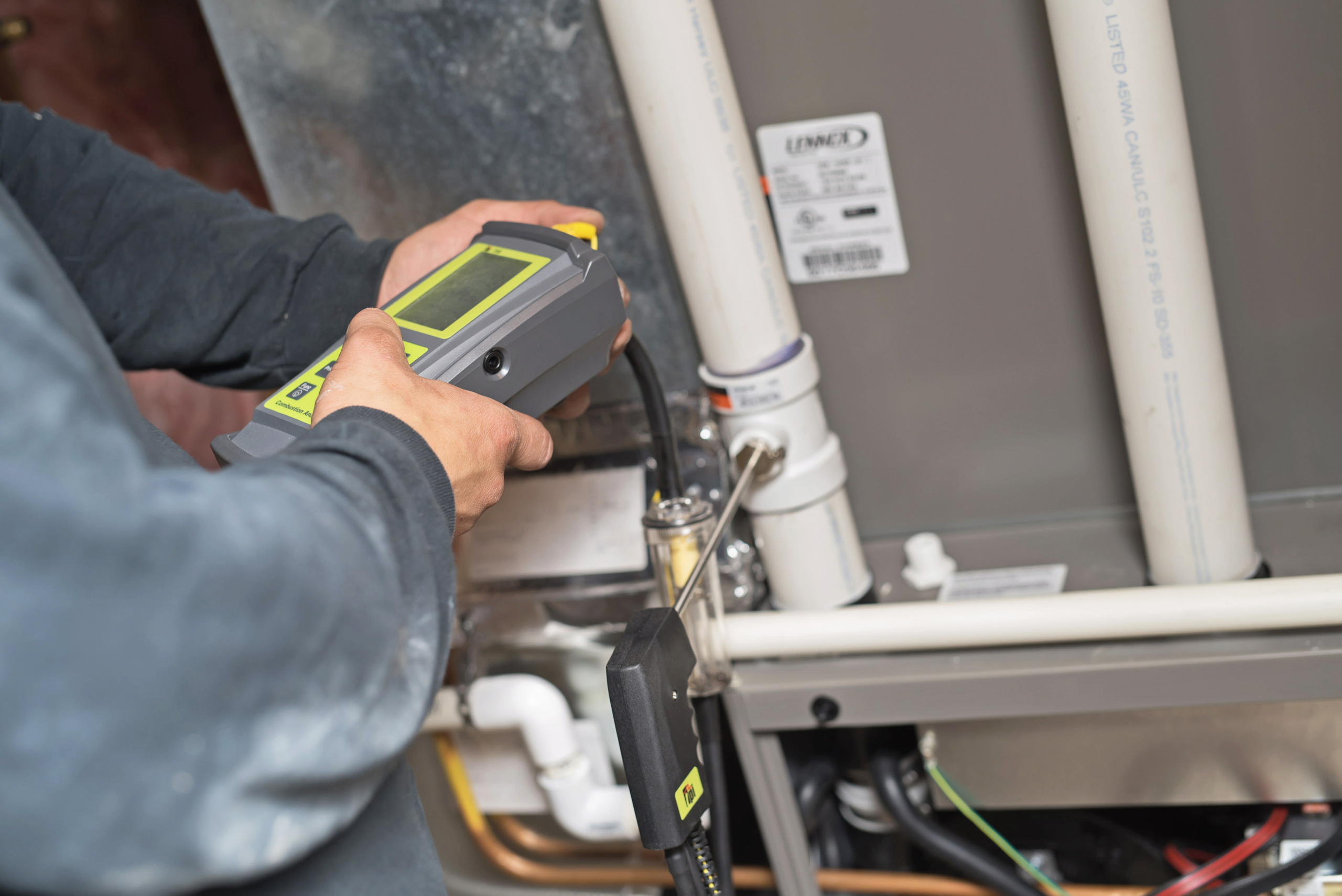 A person uses an electronic device to inspect or test pipes and connections on furnaces or HVAC systems, checking for issues or performing maintenance.